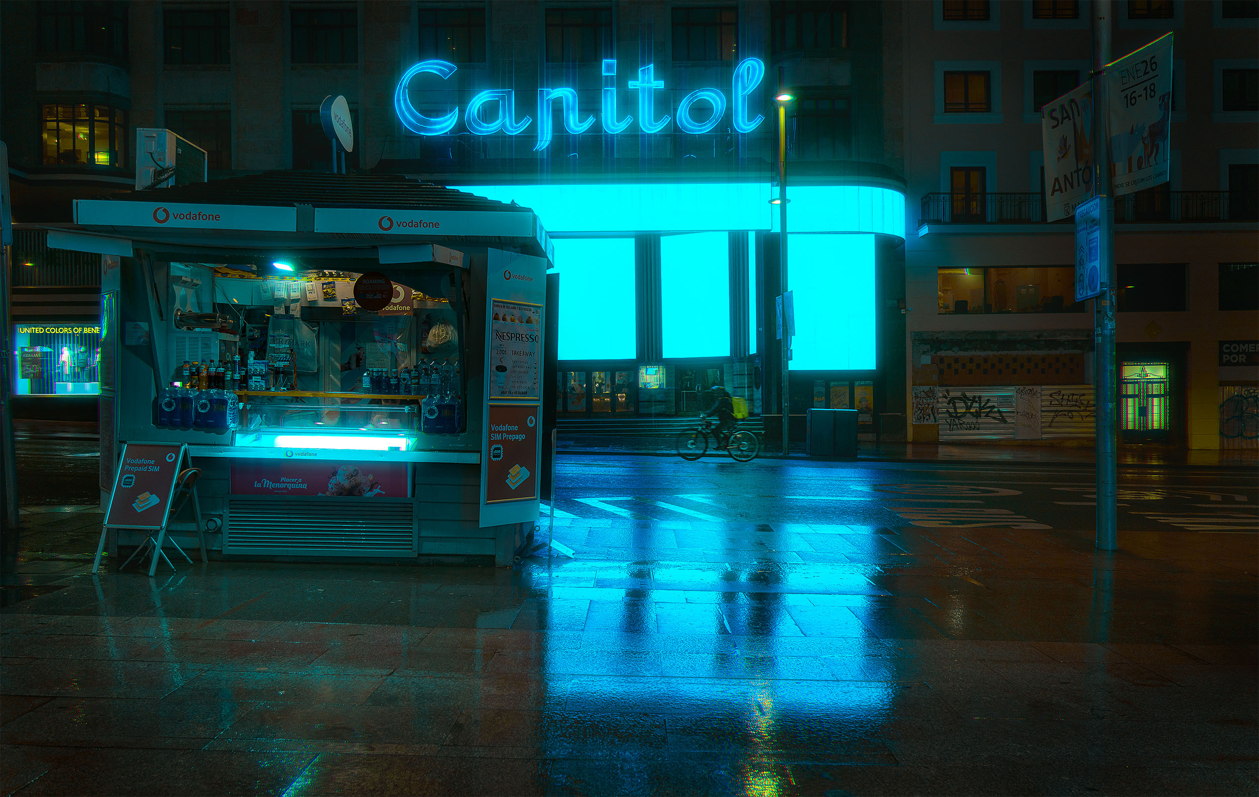 Street kiosk and Capitol building at night in Madrid, dominant cyan neon light reflecting on rain-soaked pavement, cyclist in the background