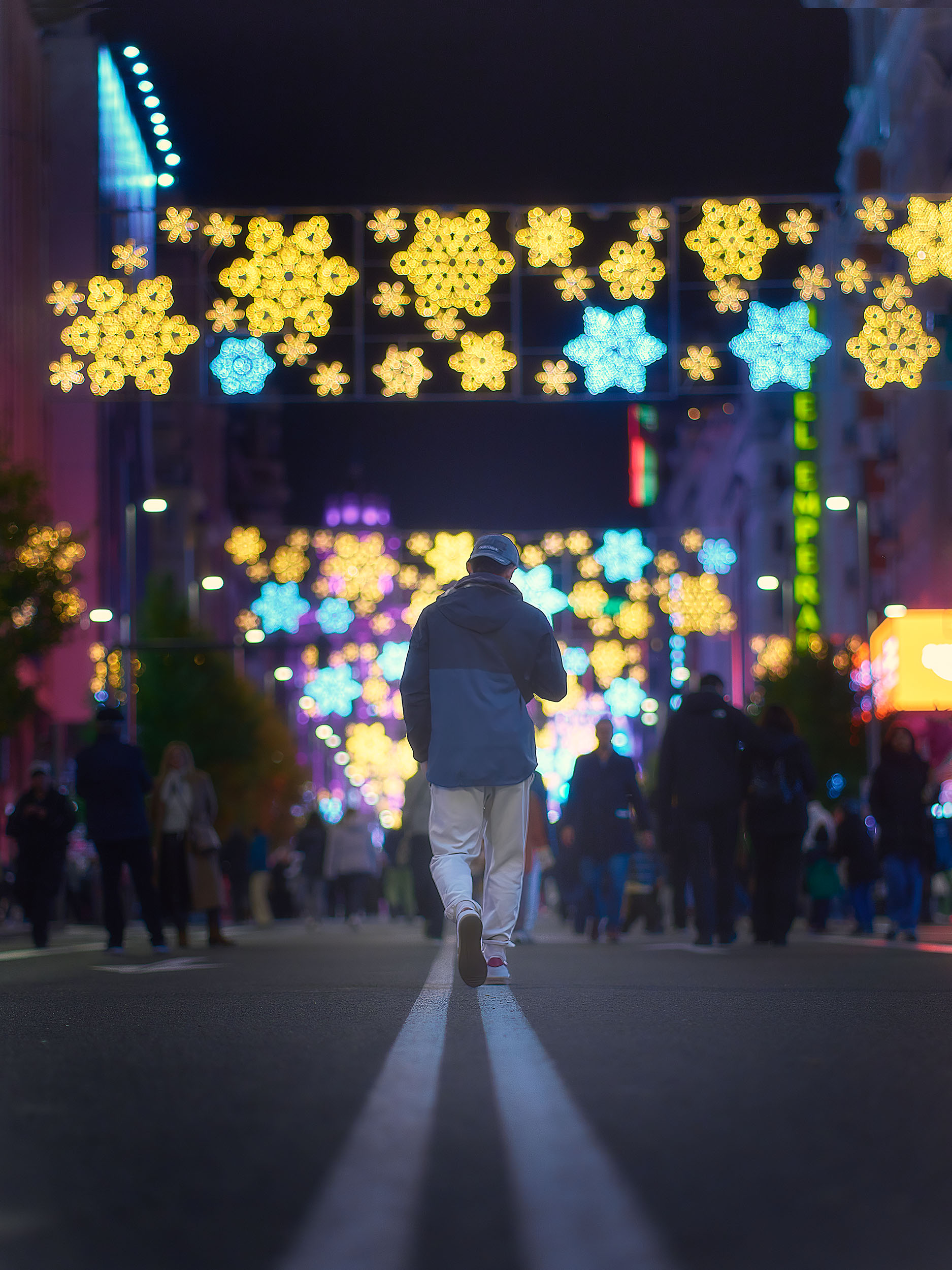 Lone figure walking towards Christmas snowflake lights on Gran Vía, Madrid, at night, colorful bokeh and purple atmosphere