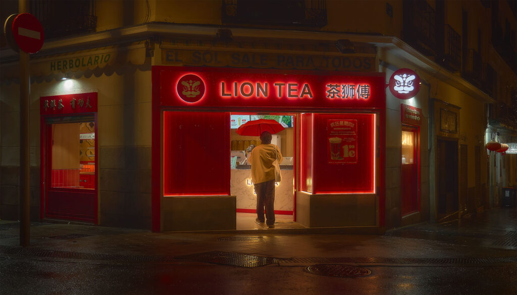 Person with red umbrella standing at the entrance of Lion Tea shop at night, intense red neon light reflecting on wet Madrid street