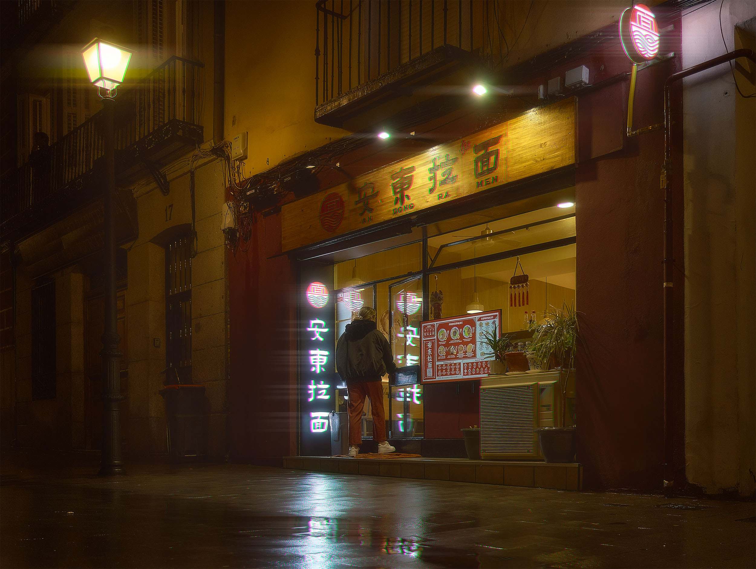 Person entering a neon-lit ramen restaurant on a rainy night, Madrid, Spain