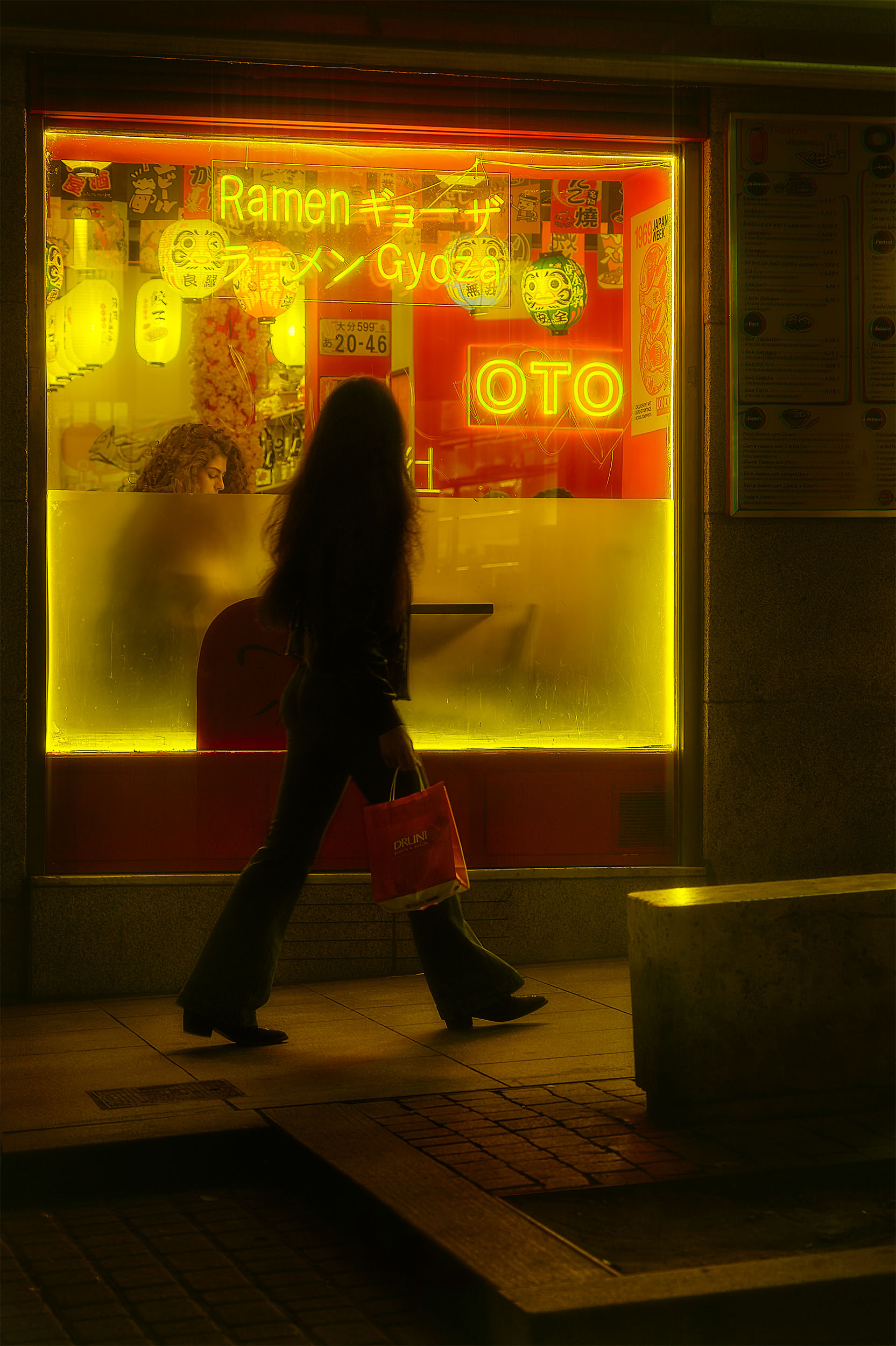 Silhouette walking past a glowing ramen shop window at night, Madrid, Spain