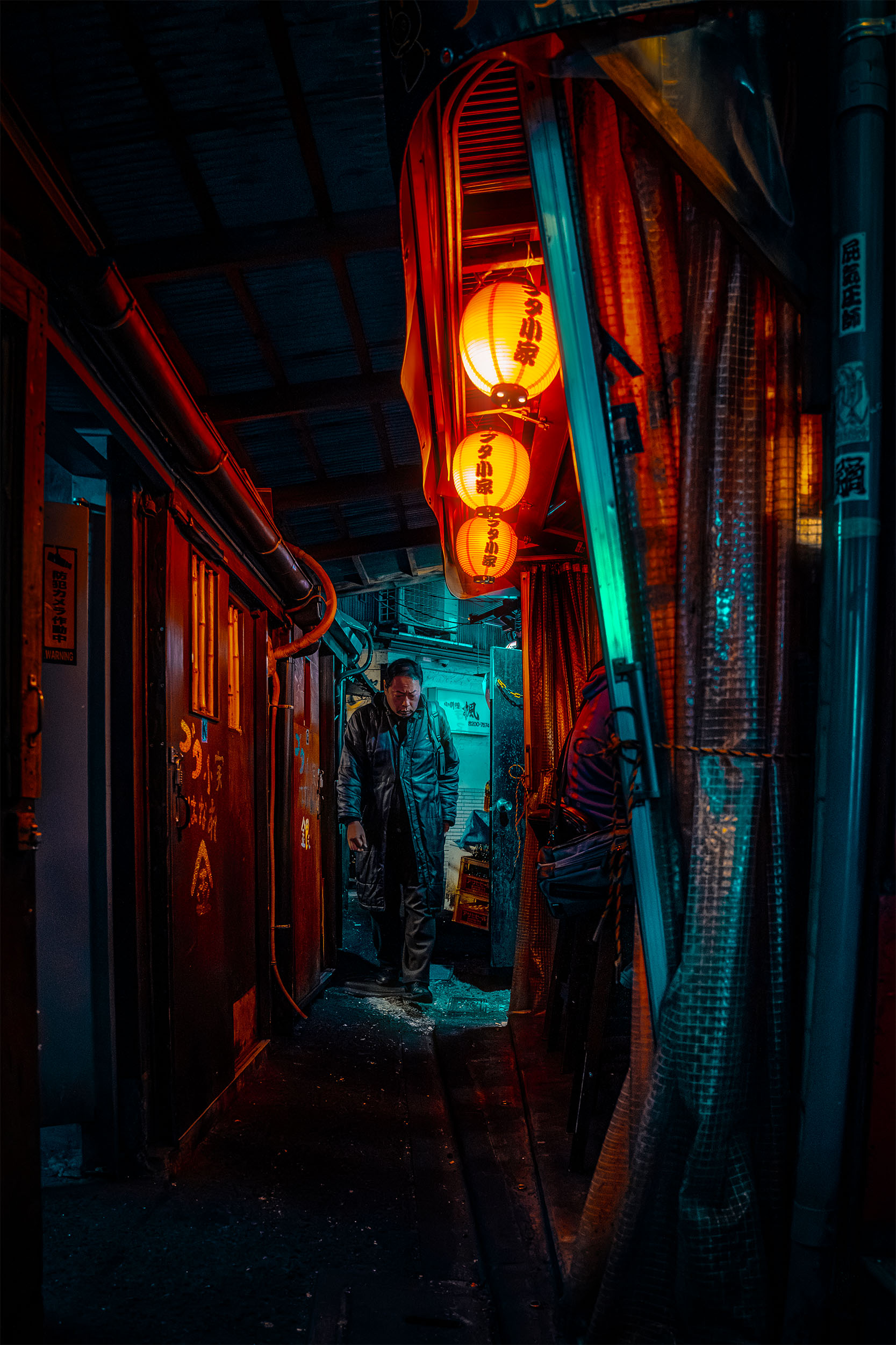 Lone figure walking through a narrow alley in Kabukicho at night, Tokyo, Japan, orange paper lanterns glowing overhead, red and teal atmospheric light, cyberpunk street photography